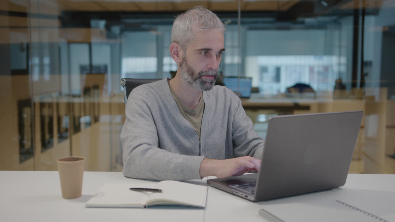 Senior Businessman Working on Laptop and Taking Notes in Office