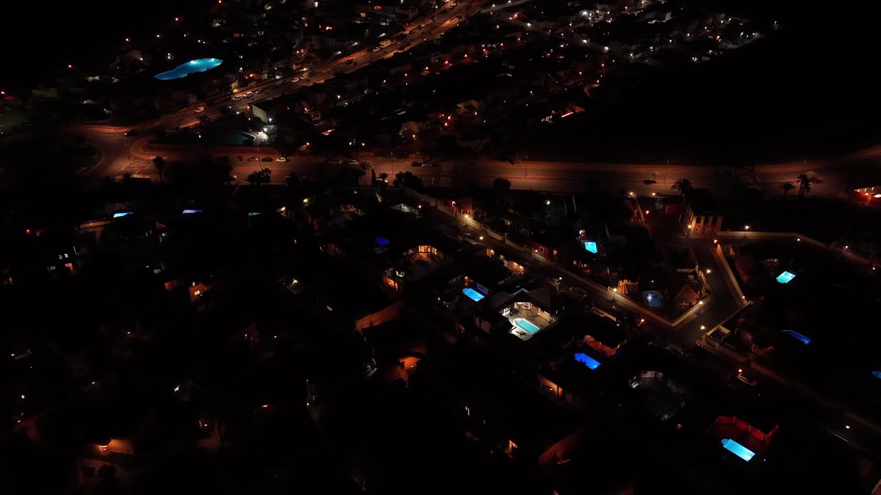 Drone orbit over a residential villa at night in Fuerteventura, Canary Islands, showcasing illuminated pools, streetlights, and the quiet rhythm of island living