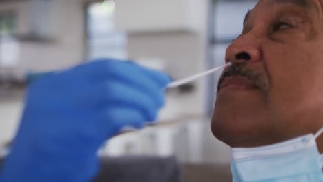 médico de raza mixta que usa una máscara haciendo una prueba de hisopo en un hombre mayor en casa