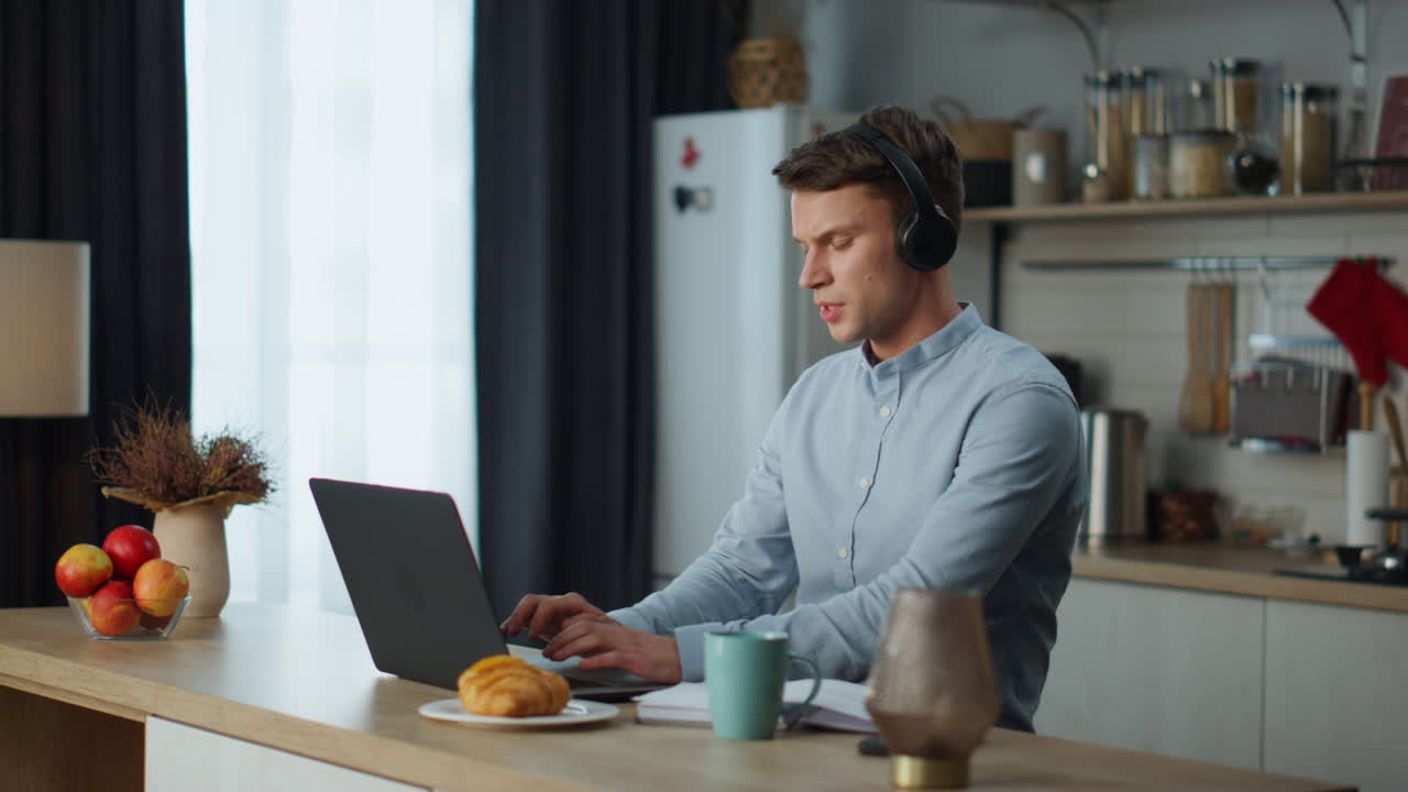 Student studying online laptop at kitchen with headphones. Man listening webinar