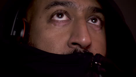 close up shot of bangladeshi gamer wearing headset and hoodie zipped up to mouth, looking with eyes