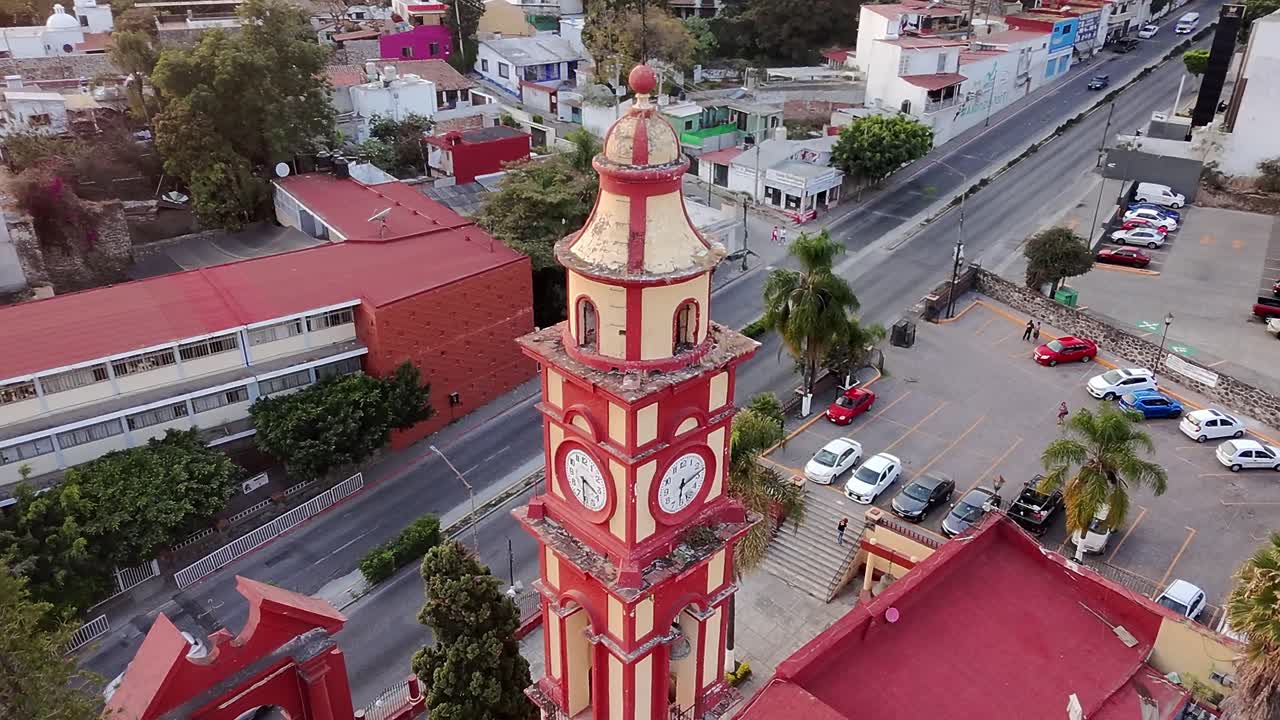 A clock tower stands tall in the heart of the city, with colorful buildings and cars surrounding it