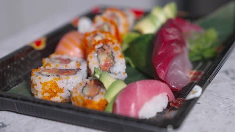a roaming shot showing assorted sushi rolls being placed into a to-go box, perfect for showcasing sushi takeout, food packaging, and delivery services in a restaurant or culinary setting.