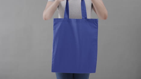 mujer caucásica con camiseta blanca sosteniendo una bolsa azul sobre un fondo gris, espacio de copia, cámara lenta