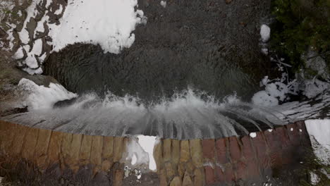 aerial top down view of flowing waterfall along stelvio pass with clear, cascading water and melted snow