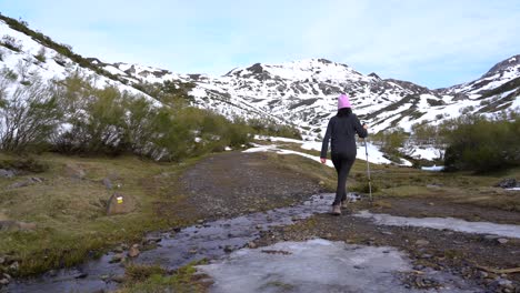 mujer cruzando un arroyo helado en las montañas mientras camina