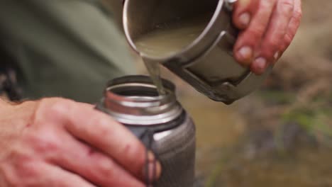 manos de un sobreviviente caucásico vertiendo agua de arroyo en una botella de filtro para beber