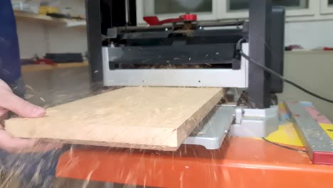 primer plano de un carpintero masculino usando una cepilladora de espesor para aplanar tablones de madera