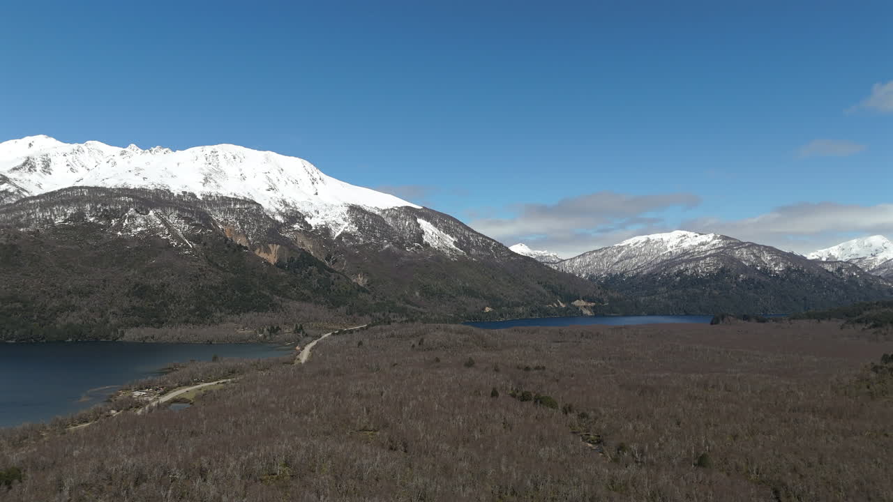 Drone shows road between Lago Villarino and Lago Falkner, forest surrounding lakes, snow covered Cerro Falkner mountains - Neuquen Province, Argentina