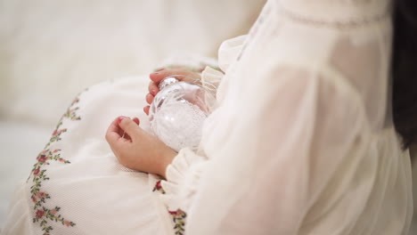 Over-the-shoulder-of-little-girl-in-a-Christmas-white-dress-holding-a-white-transparent-bauble---close-up