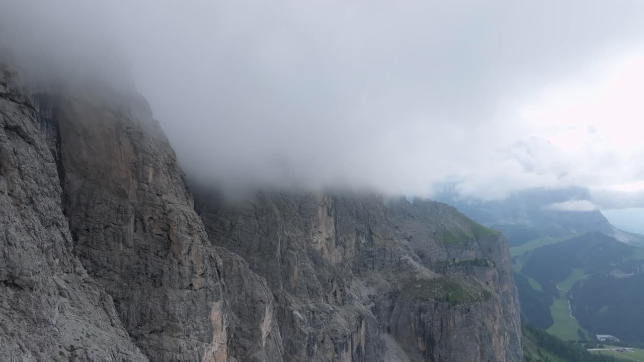 un dron aéreo se desliza hacia adelante, revelando los escarpados picos de paso gardena envueltos en nubes