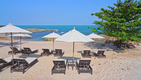 white sand beach with free comfortable lounges and white umbrellas near the ocean or sea during bright sunny day