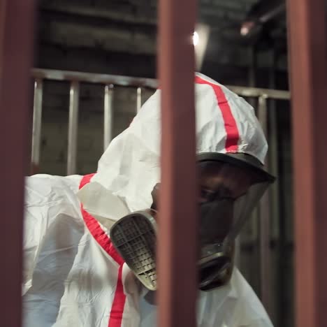 Man in white protective suit and mask paints metal structure.Worker in respirator using a spray gun to paint metal frame in a workshop. Production facility.