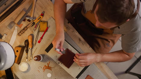 worker pierces leather with awl and round hammer at table