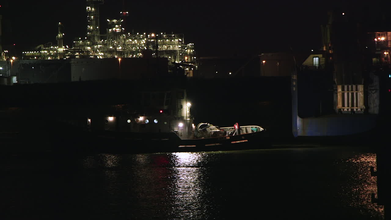 Tugboat at Night Near an Illuminated Industrial Refinery