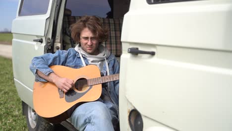 a young guy with glasses plays the guitar in the back of a caravan.