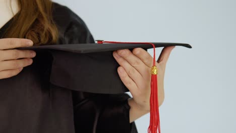 a square black hat with a red brush in the hands of a caucasian graduate with neat natural nails. close-up shooting of a hat and hands. white background