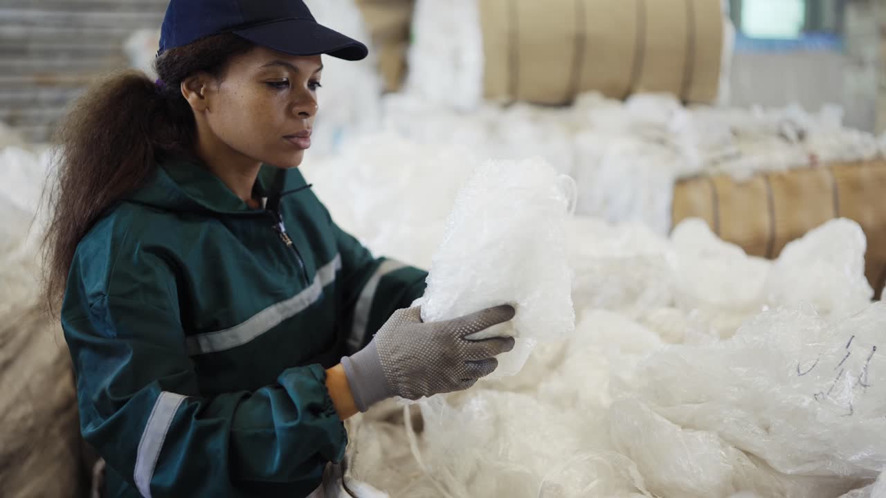 An African-American woman in a special uniform sorts polyethylene at a waste recycling plant. Processing of raw materials, recycling. Pollution control