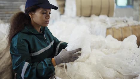 una mujer afroamericana con un uniforme especial clasifica polietileno en una planta de reciclaje de residuos. procesamiento de materias primas, reciclaje. control de la contaminación