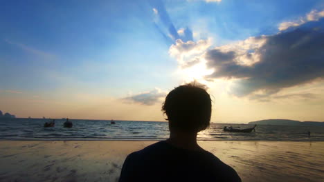 man filmed from behind walking towards the beach in slow motion at sunset