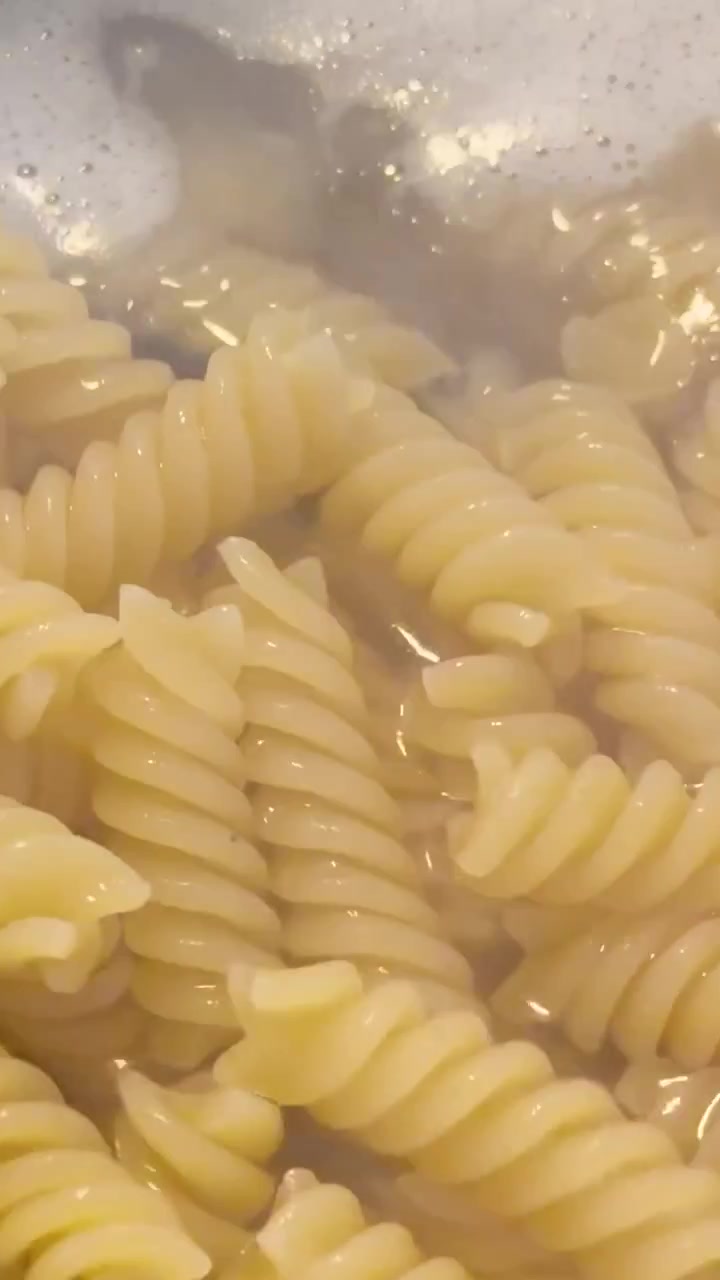 Scatto macro verticale di pasta fusilli a spirale che cuoce in acqua bollente con vapore che sale