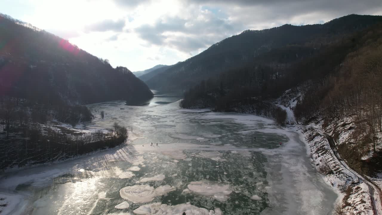 A frozen river surrounded by snowy mountains under a cloudy sky, serene and cold