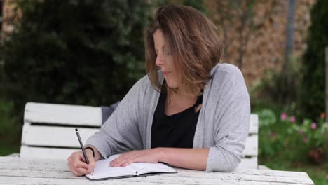 natural caucasian women writes in her journal sitting in the garden on a white table