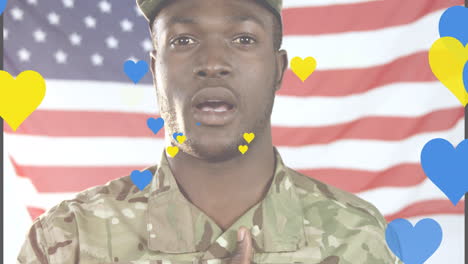 animation of yellow and blue hearts over african american male soldier singing anthem on usa flag