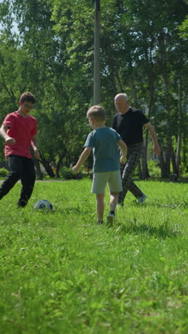 grandchildren are playing with a soccer ball in a grassy field as their grandfather joins in, trying to get the ball