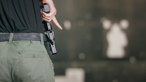 back view close-up of a man returning a pistol to its holster after firing a shot at an indoor target range