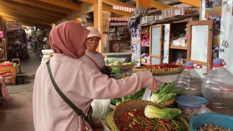 a woman wearing a hijab is buying organic vegetables sold by a vegetable trader at a traditional market.