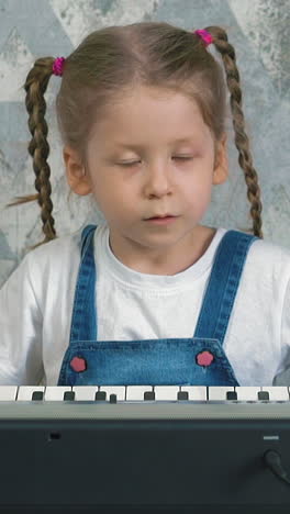 slow motion portrait of little girl at home in quarantine play on electric piano sad slow song, child in blue sundress, white t-shirt, with long blond hair braided in pigtails