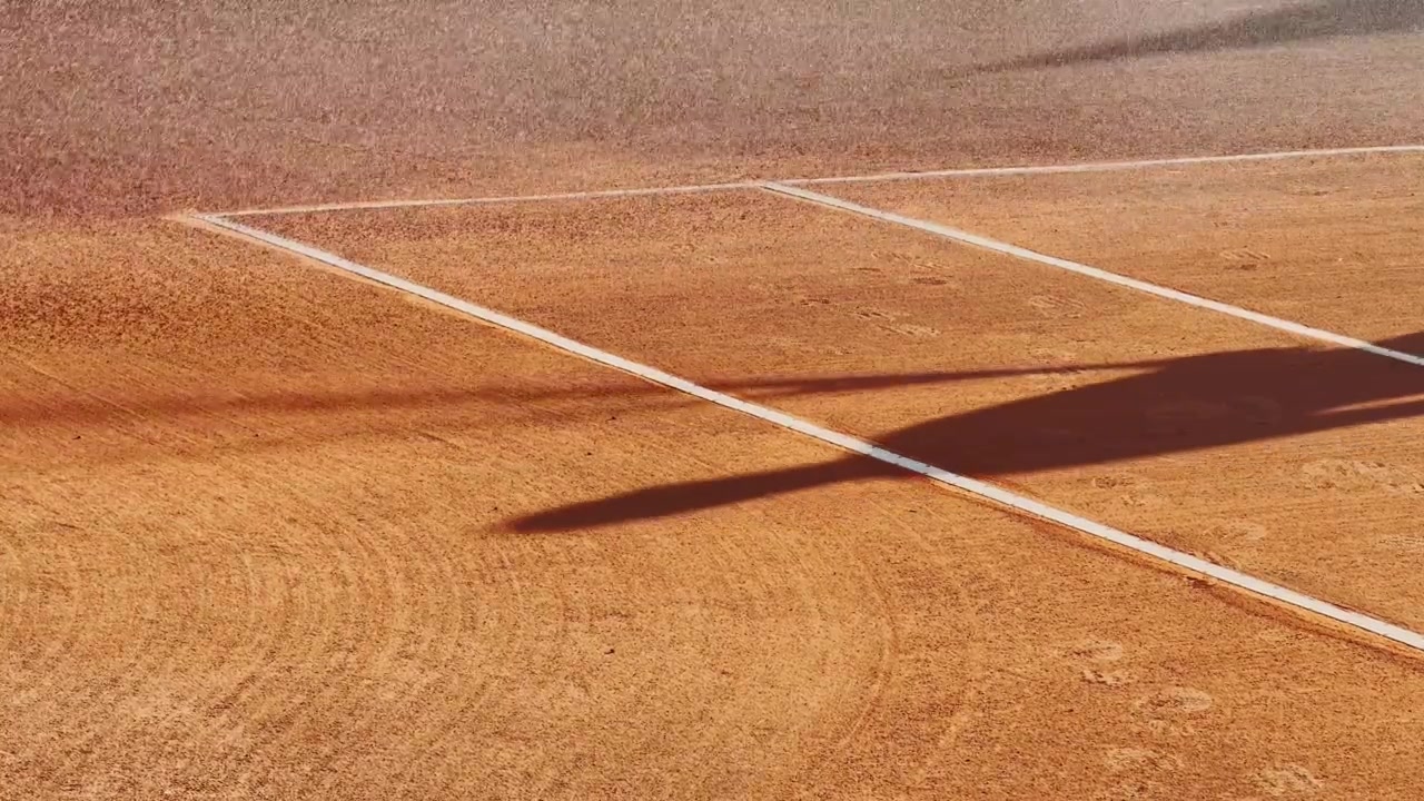Grustennisbane vannes før spill, med våt oransje overflate, hvite sidelinjer og vedlikeholdsforberedelser for en sportskamp.