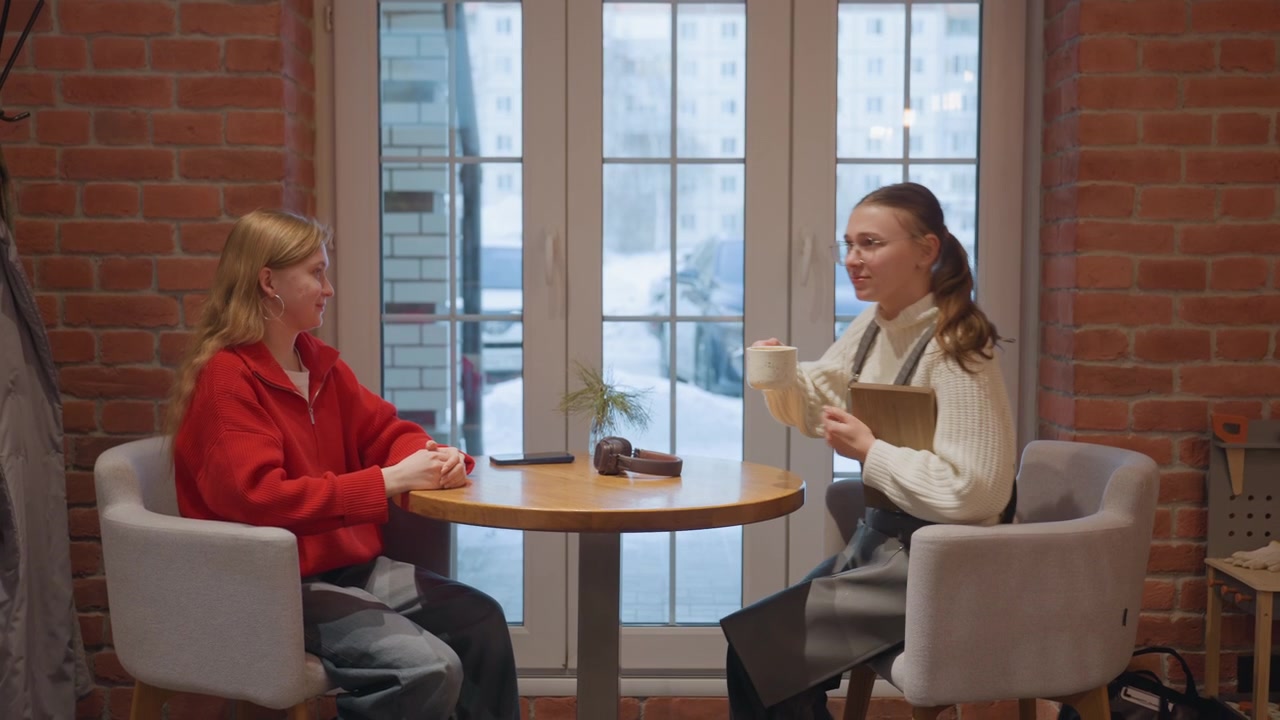 Två unga kvinnor har en avslappnad konversation på ett mysigt kafé