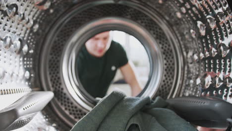 view looking out from inside washing machine as man puts in laundry load