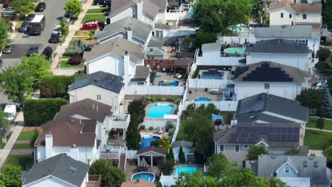 aerial orbit shot of american residential area with swimming pools in garden and driving cars on road during sunny day in summer - installed solar panels on roof producing green energy