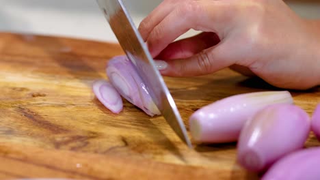 a close-up view of a hand skillfully slicing shallots on a wooden board with a sharp knife.