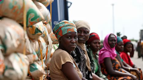 nigerian women wearing colorful traditional clothing are patiently waiting near large sacks of food aid, embodying resilience and hope in challenging circumstances