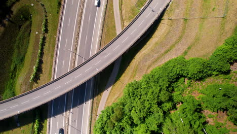 Aerial-top-down-view-of-vehicles-running-on-highway-and-crossing-under-overpass-on-bright-sunny-day