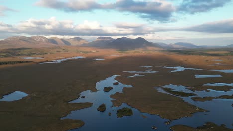 wide aerial shot of connemara lakes with calm lakes in the foreground and beanna beola mountain range in the distance, slowly rotating drone shot