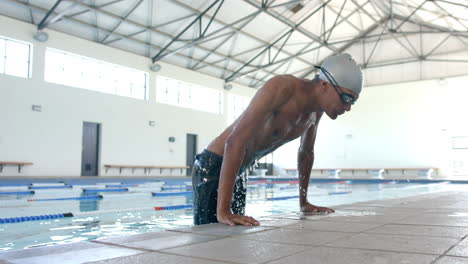 young biracial male athlete swimmer at the poolside, ready for a swim