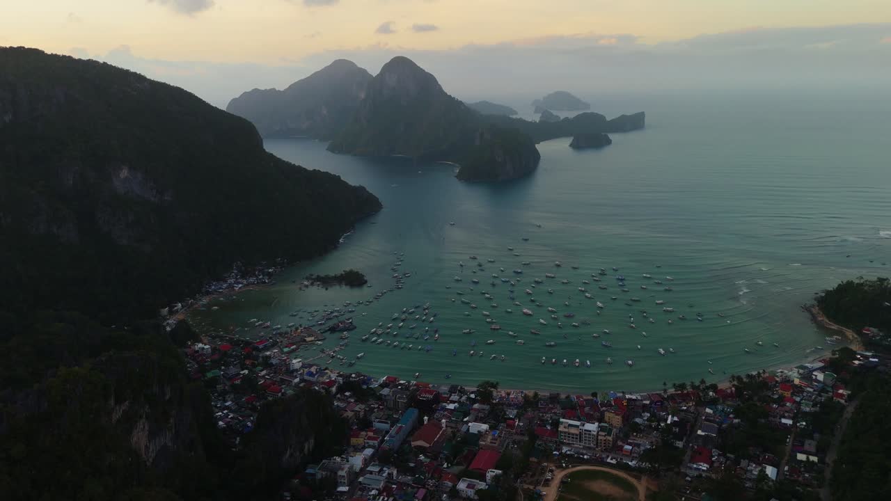 Góc nhìn điện ảnh từ drone về vịnh El Nido ở Palawan, Philippines. Cảnh quay góc cao hàng trăm chiếc thuyền buồm neo đậu gần thị trấn, được bao quanh bởi những vách đá vôi biểu tượng lúc hoàng hôn.