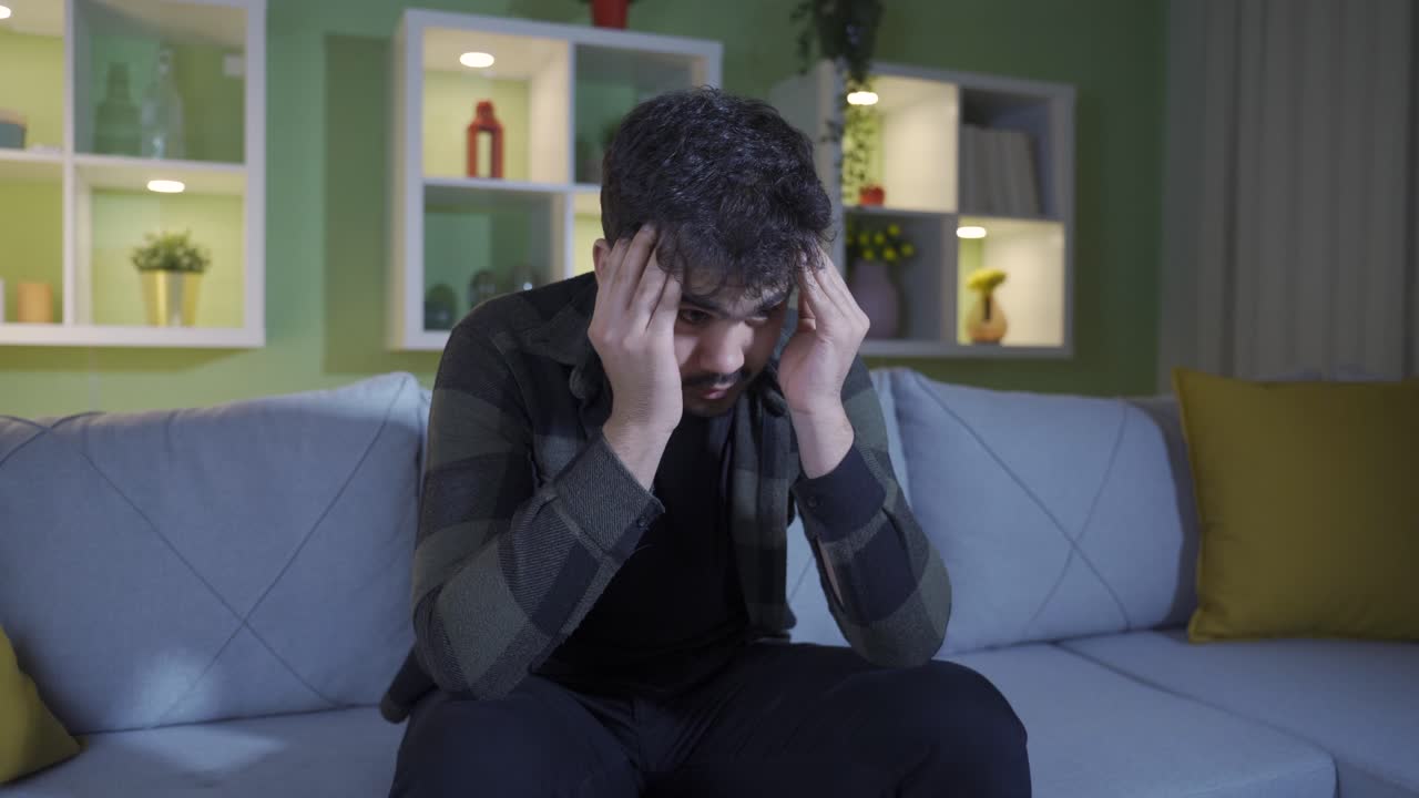 걱정하고 스트레스를 받는 젊은 남자가 집에서 혼자 생각하고 긴장하고 있습니다.