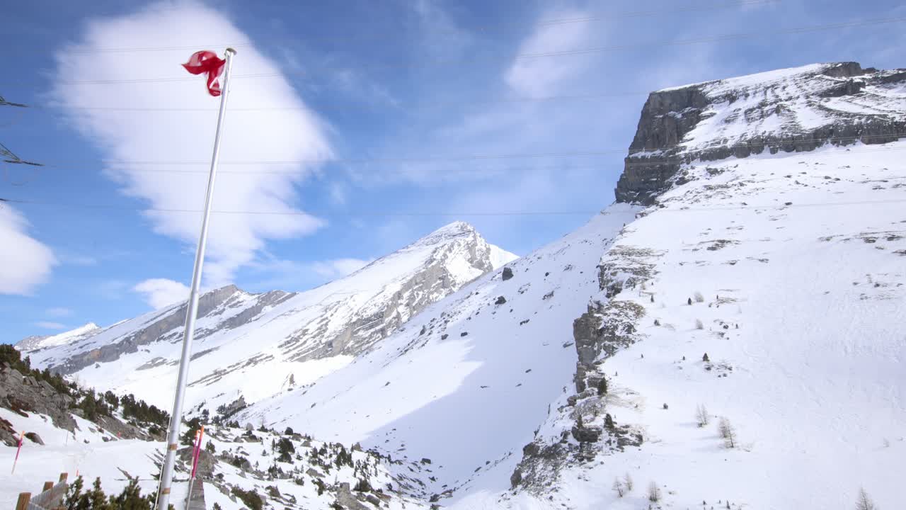 Swiss flag moving in strong wind in winter mountain landscape