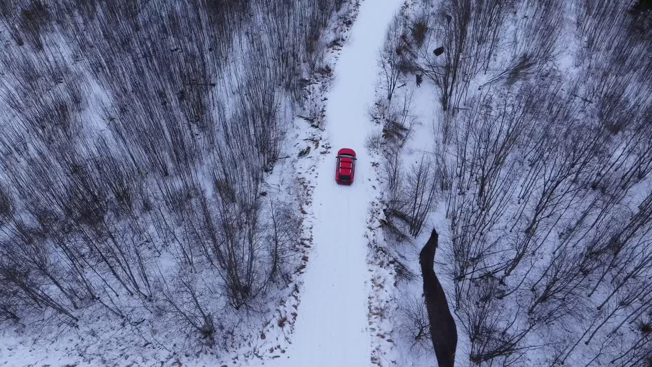 Top down drone tracks red car along icy forest road in silent Northern winter