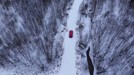 top down drone tracks red car along icy forest road in silent northern winter