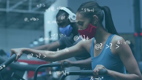 Animation-of-symbols-changing-over-woman-and-man-in-face-masks-exercising-on-elliptical-bikes-in-gym