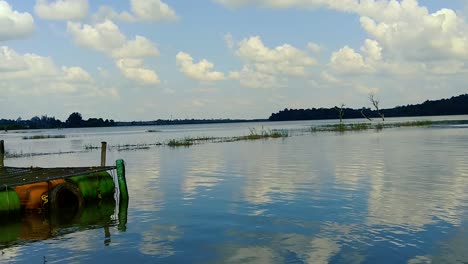 blue sky with soft white clouds reflecting on the calm surface of a small pond