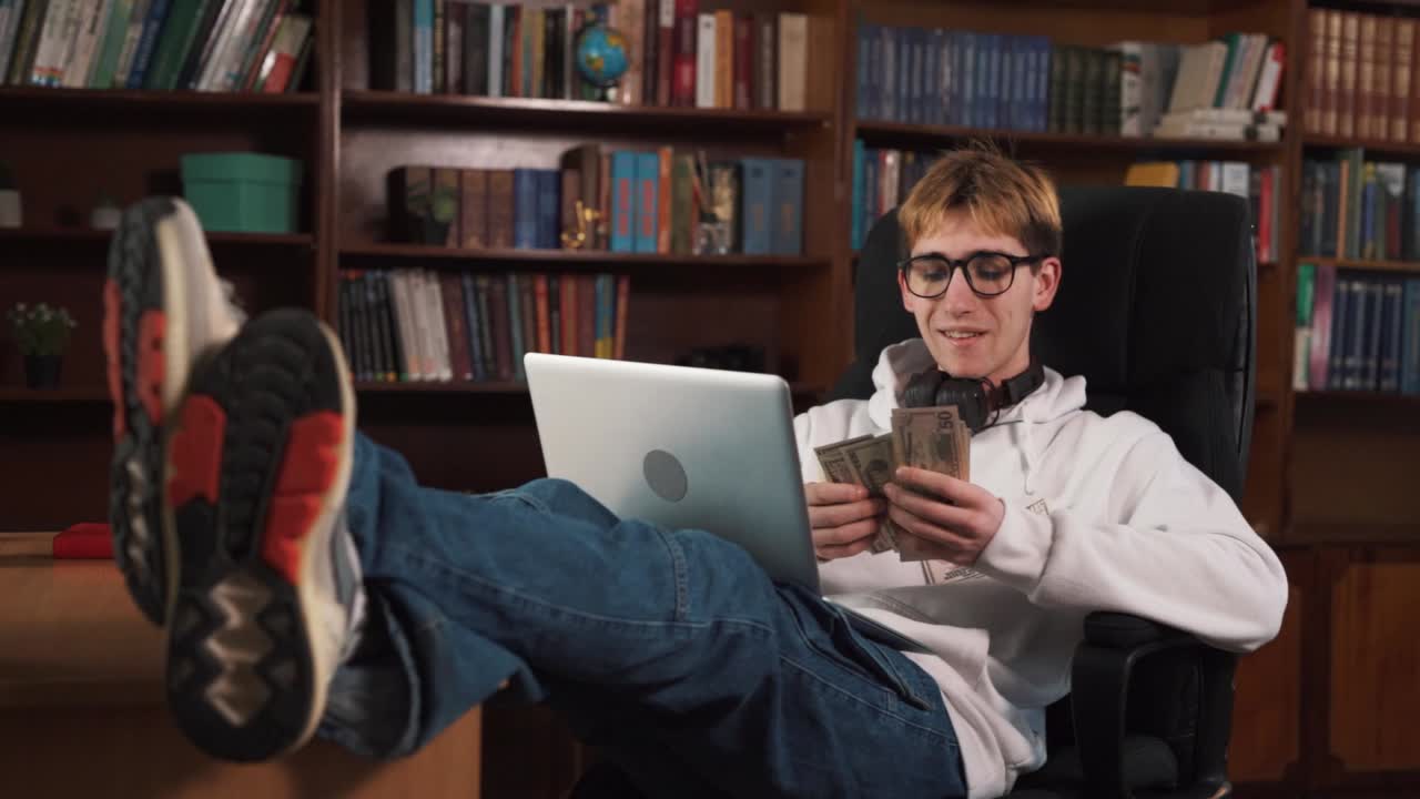 el hombre guapo está sentado en una silla, con los pies en la mesa, y tiene una computadora portátil en su regazo