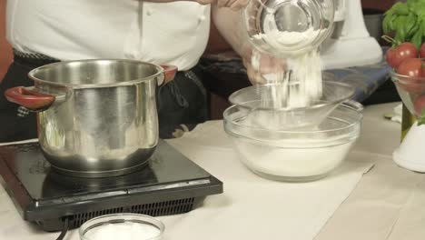 chef sifts flour in preparation for batter frying foods in pot of oil